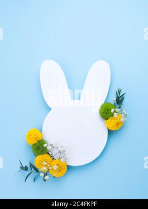 Happy Easter card. Easter bunny from white paper with flowers on light blue background with blank space for text. Top view, flat lay. Stock Photo
