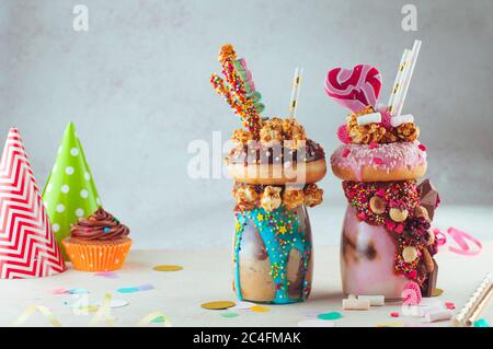 Two freak shakes topping with donut, caramel popcorn and sweets on grey background Stock Photo