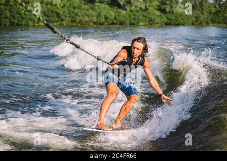 A man is surfing on a surfboard drawn by a motor boat above the wave of the boat. Weixerfer is engaged in surfing, entertainment, leisure, water Stock Photo