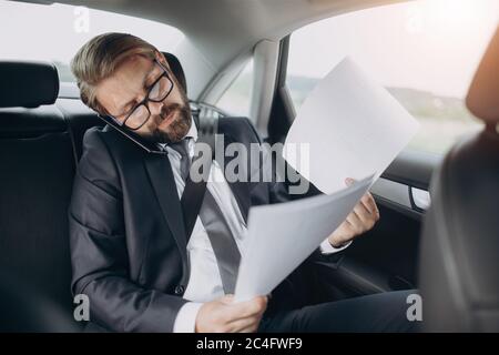 Businessman talking on phone and reading documents at car Stock Photo