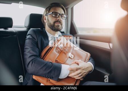 Businessman sitting in car and holding bag with documents Stock Photo