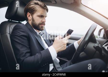 Busy man in formal suit using smartphone while driving car Stock Photo