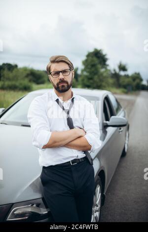 Businessman in glasses standing near car with crossed hands Stock Photo