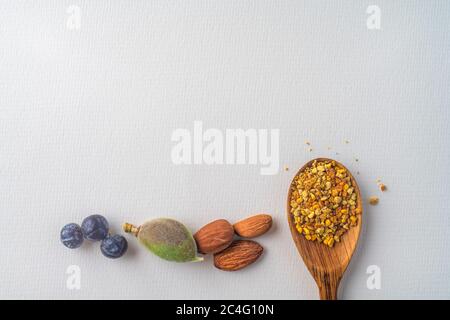 Three juniper blue old berries, almonds nut and bee pollen in wooden spoon on spring, isolated on white textured paper. Copy space. Balanced diet