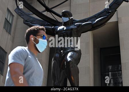 New York City, USA. 26th June, 2020. A man wearing a face masks in the time of COVID-19 walks past ATLAS, a bronze statue by artist Lee Lawrie, located at Rockefeller Plaza, is adorned with a blue face mask to promote Phase Two of New York City's reopening and encourage social distancing to stop the spread of COVID-19, New York, NY, June 26, 2020. (Anthony Behar/Sipa USA) Credit: Sipa USA/Alamy Live News Stock Photo