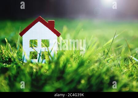 small white toy house on green grass in sunshine with copy space for real estate purchase, mortgages, homeowner insurance, house and lot for sale mock Stock Photo