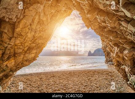 view from the stone cave on the sunset sea and the beach, the volcanic rock of the cave as in Iceland is lit by the warm setting sun. The concept of Stock Photo