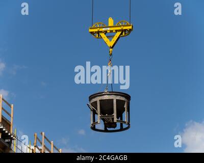 a concrete bucket hanging from a crane at a high rise construction site Stock Photo
