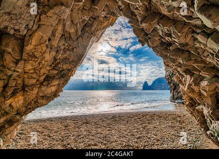 view from the stone cave on the sunset sea and the beach, the volcanic rock of the cave as in Iceland is lit by the warm setting sun. The concept of Stock Photo