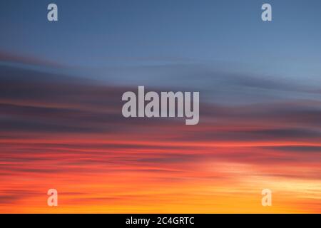 Intense, radiant orange cirrus clouds at dawn against a deep blue sky. Stock Photo