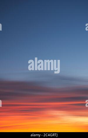 Intense, radiant orange cirrus clouds at dawn against a deep blue sky. Stock Photo