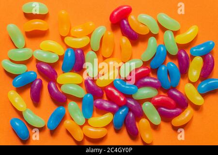 Multi-colored glazed jelly beans sweets on orange paper background. Stock Photo