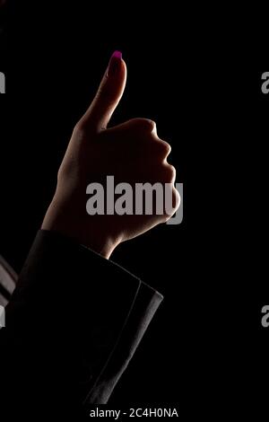 female's hand on a dark background, showing thumbs up Stock Photo