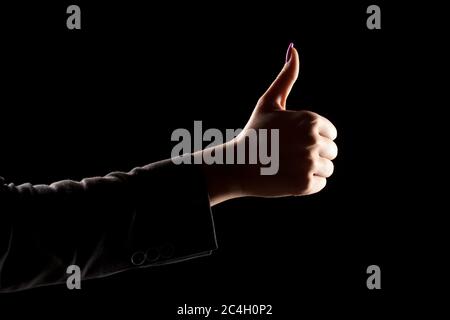 female's hand on a dark background, showing thumbs up Stock Photo