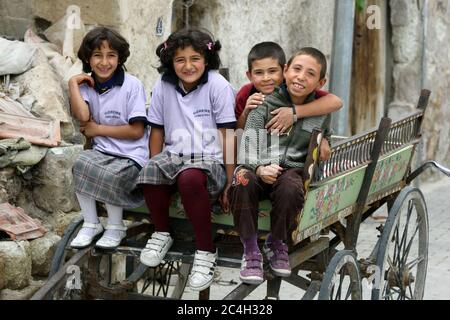 Smiling children sit in a wooden cart in the village of Goreme located in the Cappadocia region of Turkey. Stock Photo