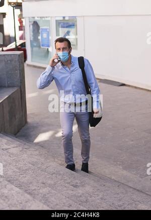 Vertical photo of a man in a formal dress with a mask on his face and a suitcase climbing a stairs while is using the phone Stock Photo