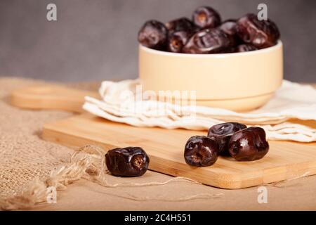 Some dates in a light yellow ceramic bowl and some dates around it on a wooden and sacking surface. Ramadan dates. Stock Photo