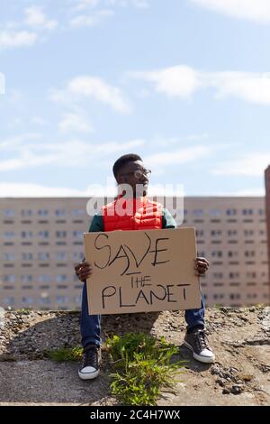 African young man sitting on stone and holding placard in his hands he protecting the nature Stock Photo