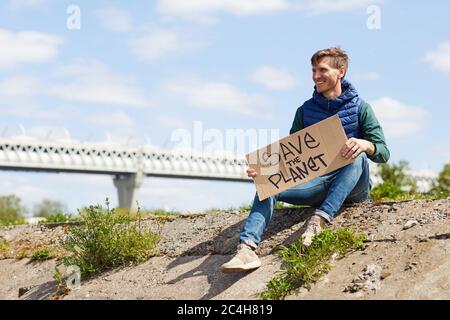 Young man working as a volunteer he holding placard and looking away while sitting outdoors Stock Photo