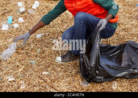 Close-up of young woman picking up the garbage into the bag outdoors Stock Photo