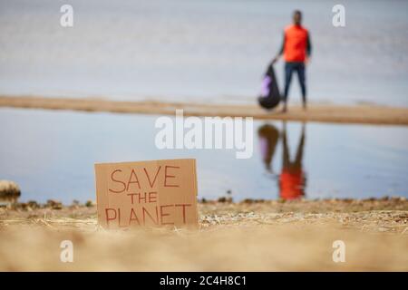 Image of placard Save the planet on the beach of the sea with man standing in the background Stock Photo