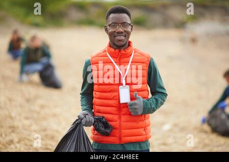 Portrait of African young man holding bag with garbage and smiling at camera while standing outdoors Stock Photo