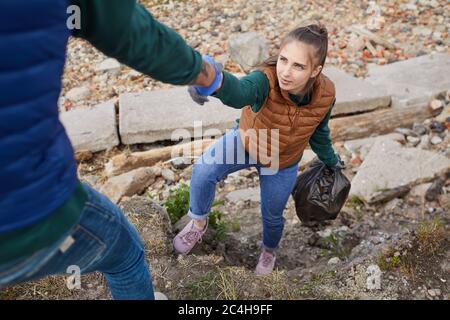 Man helping young woman up while they picking up garbage outdoors Stock Photo