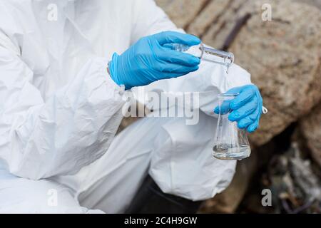 Close-up of woman in protective gloves and suit holding flasks and taking samples of water Stock Photo