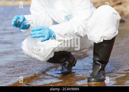 Close-up of chemist in protective workwear and in gloves holding flask and examining the water in the river Stock Photo