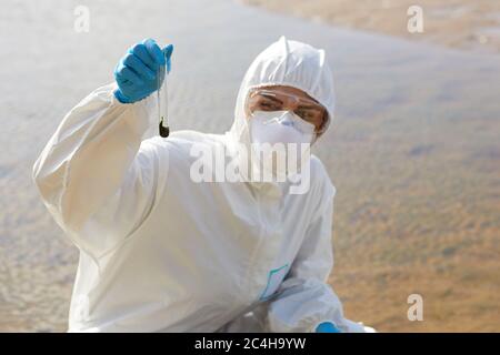 Young chemist in protective workwear holding flask with samples and working outdoors Stock Photo
