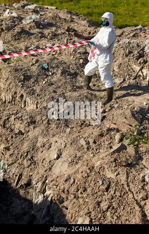 Chemist in protective suit separating dangerous area with a tape outdoors Stock Photo