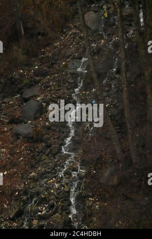 a small waterfall flowing through the rocks. waterfall having rocks and trees on both the sides . focus on infinity. Stock Photo