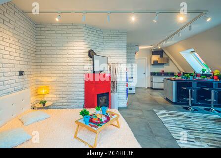 Modern loft interior of flat. Luxury studio apartment with furniture. Set table. TV on the fireplace. Brick wall. Tray on the bed. Stock Photo
