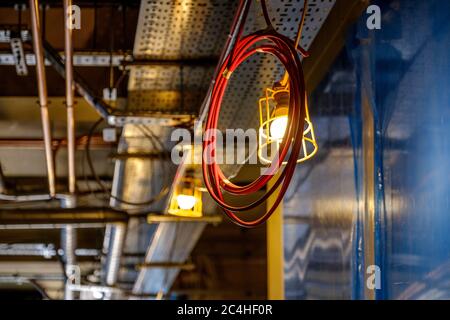 Coil of electrical cable hangs from ceiling by work light in building under construction Stock Photo