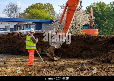 Construction worker in hard hat and hi-vis vest guides excavator on construction site Stock Photo