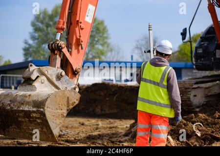 Worker in hard hat and hi-vis vest holds yardstick on construction site Stock Photo