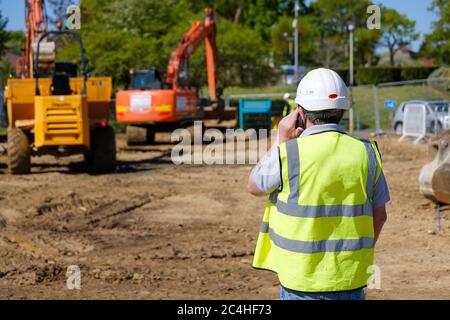Construction worker in hi-vis vest and hard hat makes mobile phone call on building site Stock Photo