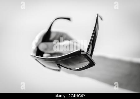 Male hand holds big stylish glasses. Blurred sunny beach background. Black and white photo. Stock Photo