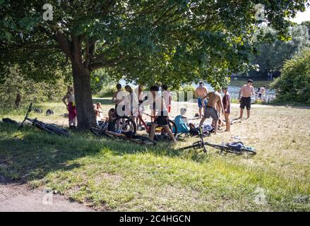 London, UK. 27th June 2020. Groups of  youths hang around the banks of the River Thames near Hampton on a hot sunny day as lockdown restrictions are eased but sensible social distancing is till required to avoid a spike in coronavirus infesctions, England, UK Credit: Clickpics/Alamy Live News Stock Photo