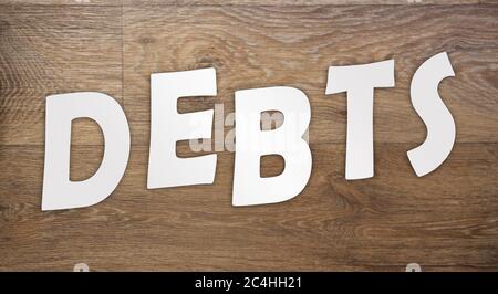 Letters cut from white paper are arranged in a word DEBTS on a wooden table. Concept of debt trap Stock Photo