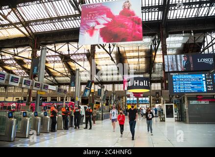 Paris, France - May 31, 2020: People in masks in Gare de Lyon train station under advertising of La vie est belle perfume ('Life is beautiful'). Stock Photo