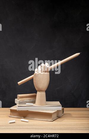 Wooden hand holding a pencil on books. Chalkboard background. Back to school concept. Copy space Stock Photo