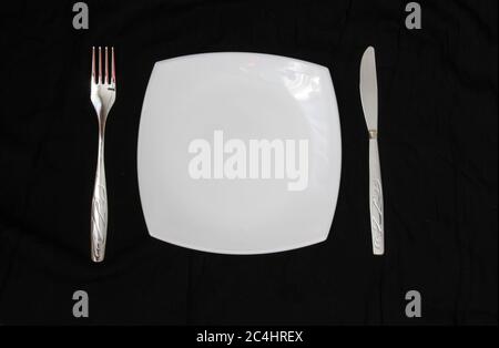 Empty plate, fork and knife over black background. Clean plate and cutlery on light background. Top view. Stock Photo