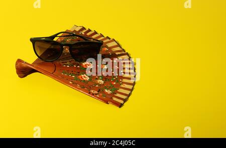 Stylish Sunglasses and Classic Spanish Hand Fan on Bright Yellow Background. . Stock Photo