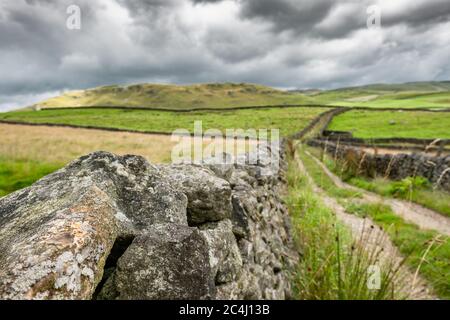 Low level view of a old dirt track leading to a valley in the Yorkshire Dales. Either side of the road is old, dry stone walling.