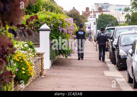 Male and female special constable police officers walking the beat in an urban area in Southend on Sea, Essex, UK, passing parked cars. Essex Police Stock Photo