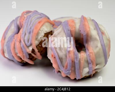 Mixed strawberry blueberry doughnut / donut covered in white glaze with pink and purple stripes of glaze on a white background.  Delicious and unhealt Stock Photo