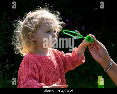 Toddler blowing bubbles with mum's help, UK Stock Photo