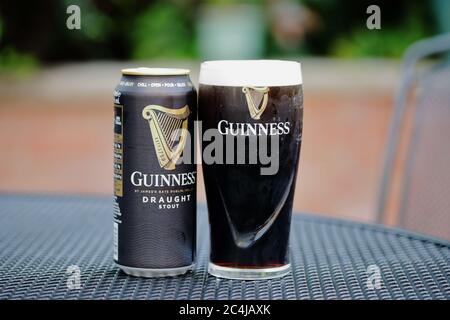 a branded glass of cold dark Guinness  poured ready to drink and a can, outside on a patio table Stock Photo