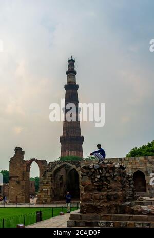 Qutub Minar, Delhi, India; 16-Aug-2019; a guy sitting on a wall with the Qutub Minar in the background Stock Photo